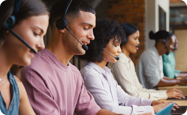 Five people wearing headsets sit in a row, diligently focused on their tasks, in an immersive virtual environment within a customer service or call center setting.