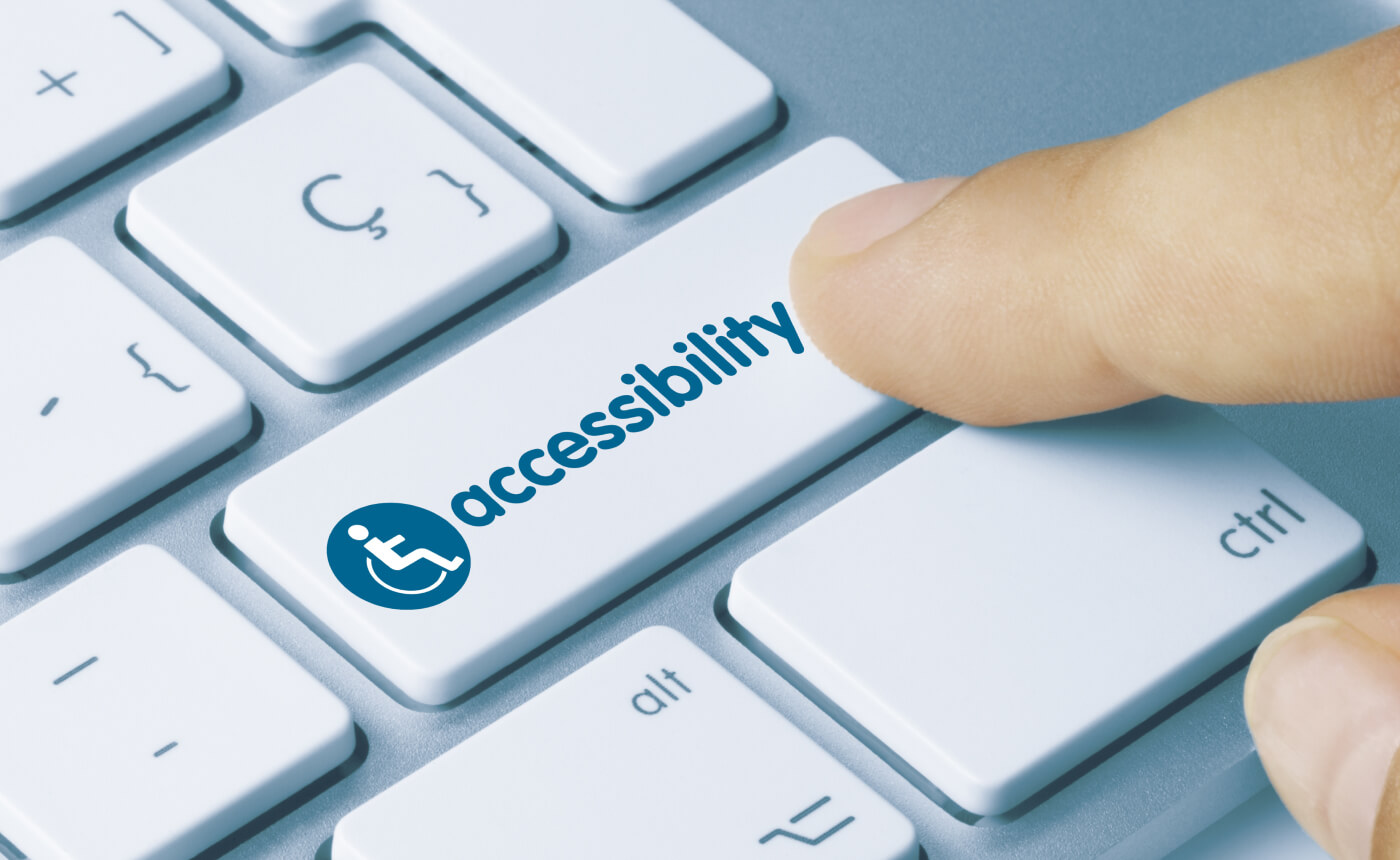 A finger presses an "accessibility" button on a white keyboard, marked with a distinct wheelchair icon, highlighting inclusivity and ease of use.