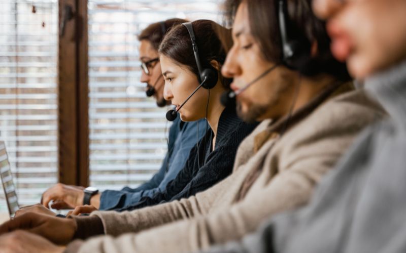 Four people wearing headsets work on laptops in a row, likely in a call center or customer service environment, supporting guests seeking accessible hotels and ensuring inclusive, accessible hospitality experiences.