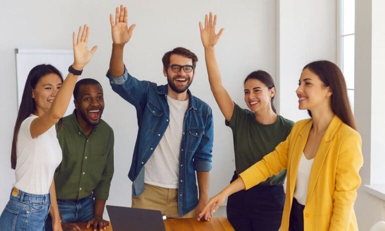 Five people standing indoors, smiling and raising their hands, appear to celebrate or participate in a corporate volunteering program