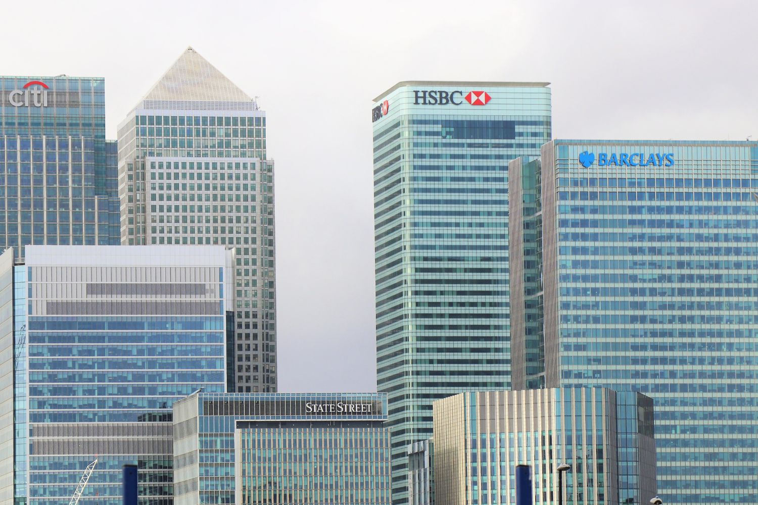 Cluster of modern skyscrapers, including Citibank, HSBC, Barclays, and State Street, standing tall against a cloudy sky.