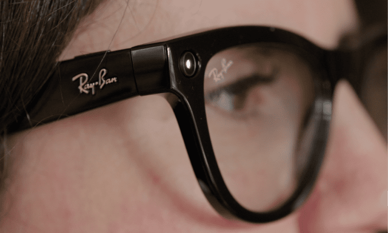 Close-up of a person wearing black Ray-Ban eyeglasses, focusing on the logo on the frame and blurred reflection in the lens.