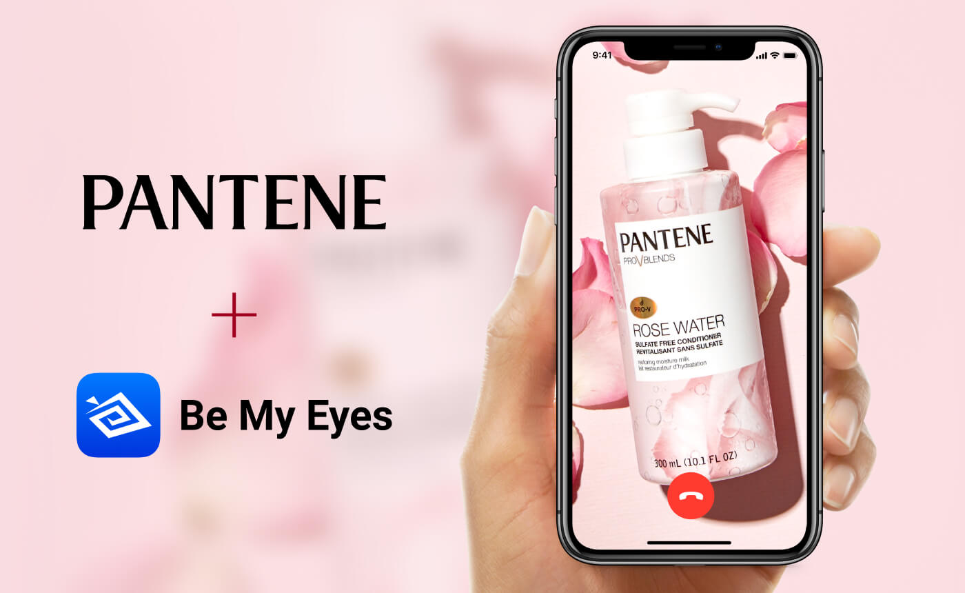 A smartphone showcases Pantene Rose Water shampoo with the text "Pantene + Be My Eyes," held gracefully against a blurred pink background.