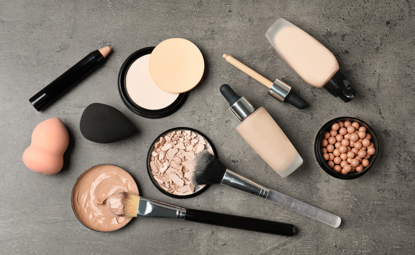A curated collection of makeup essentials, featuring foundations, powders, applicators, and brushes, is artfully displayed on a sleek gray surface.
