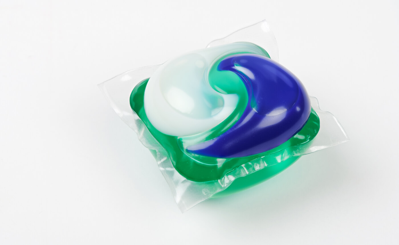 Laundry detergent pod with sections of blue, green, and white colors, encased in a transparent plastic film, on a white background.