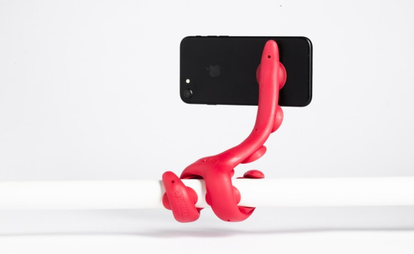 A sleek, red flexible holder grips a black smartphone securely, attached stylishly to a white bar.