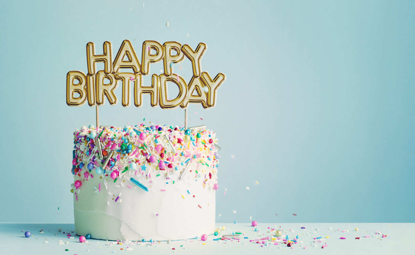 A delightful birthday cake adorned with vibrant sprinkles and a "Happy Birthday" topper sits elegantly against a light blue background, embodying the spirit of celebration.