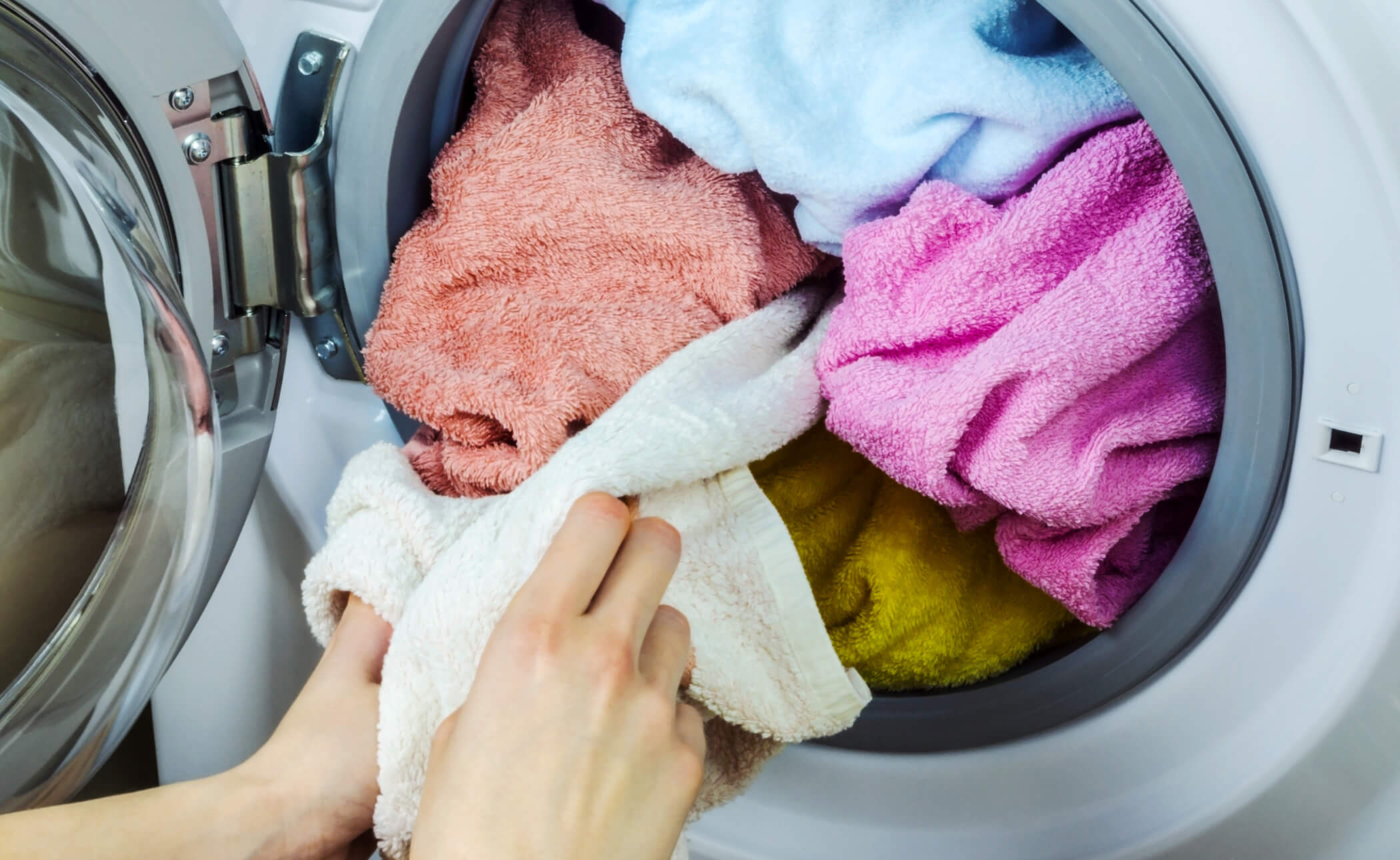 Hands carefully place vibrant towels into a front-loading washing machine, ensuring each piece fits snugly for an efficient wash cycle.