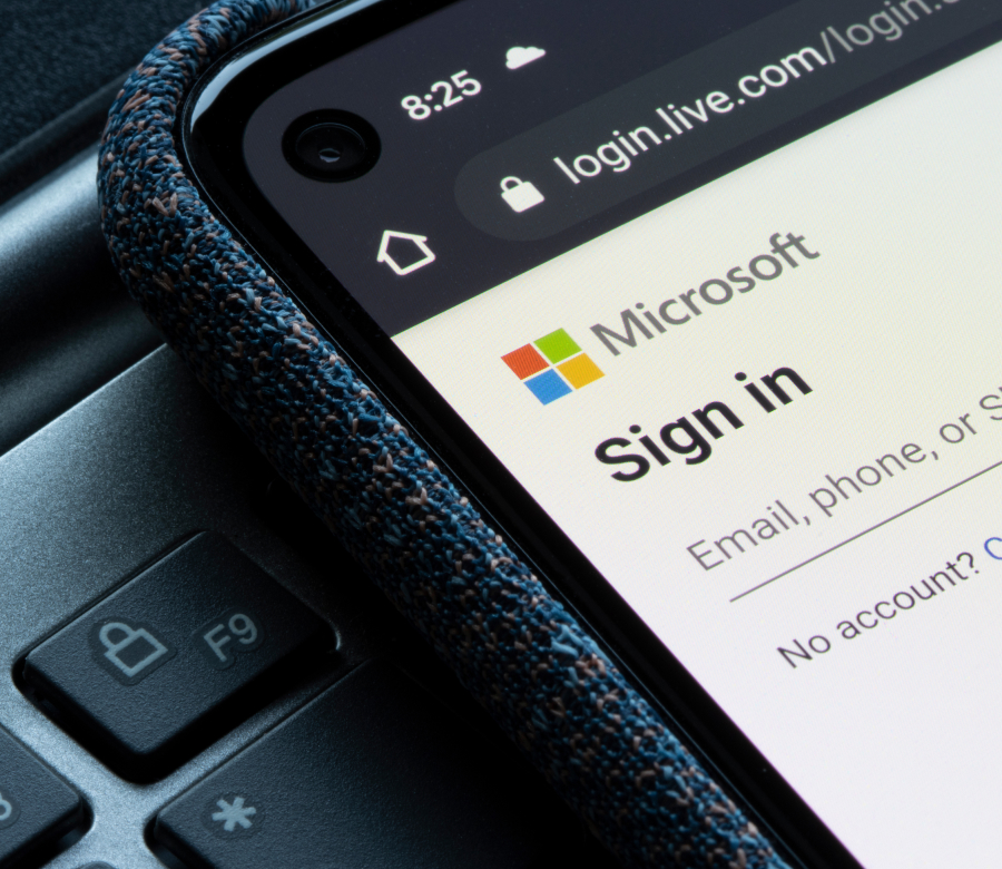 Smartphone screen displaying the Microsoft sign-in page, with login options for email, phone, or Skype. The device is resting on a laptop keyboard.