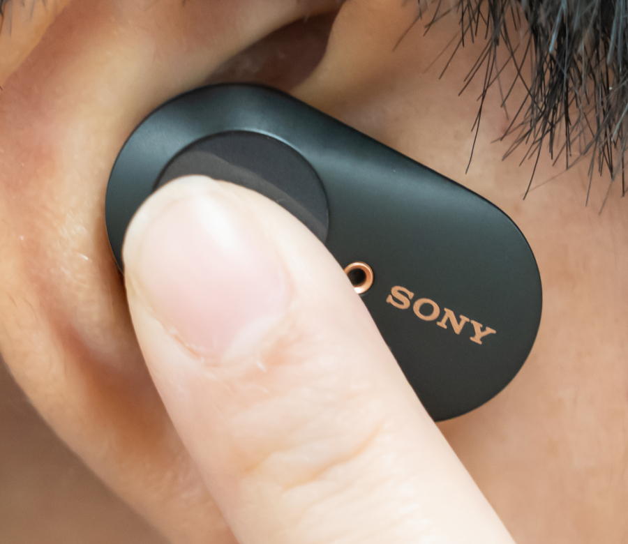 Person adjusting a black Sony wireless earbud in their ear with a finger.