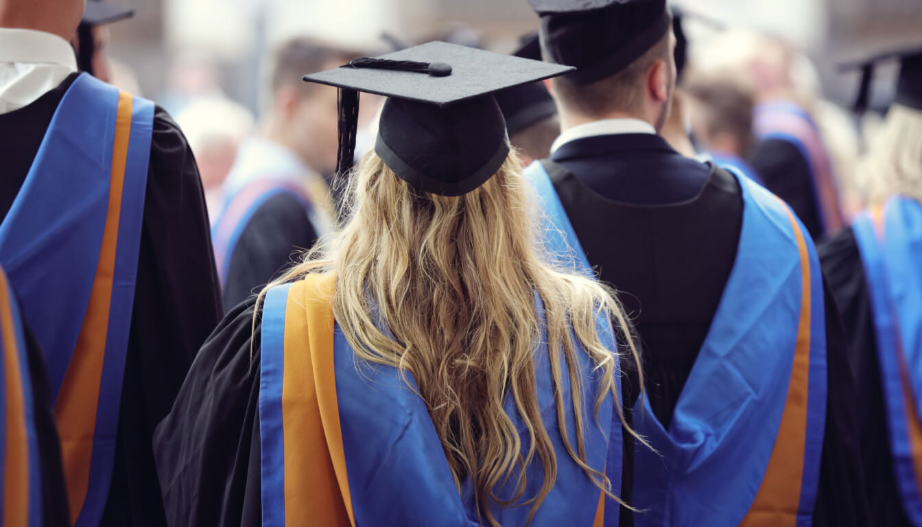 A group of graduates in caps and gowns proudly faces forward, donning vibrant blue and orange stoles as they celebrate their achievements.