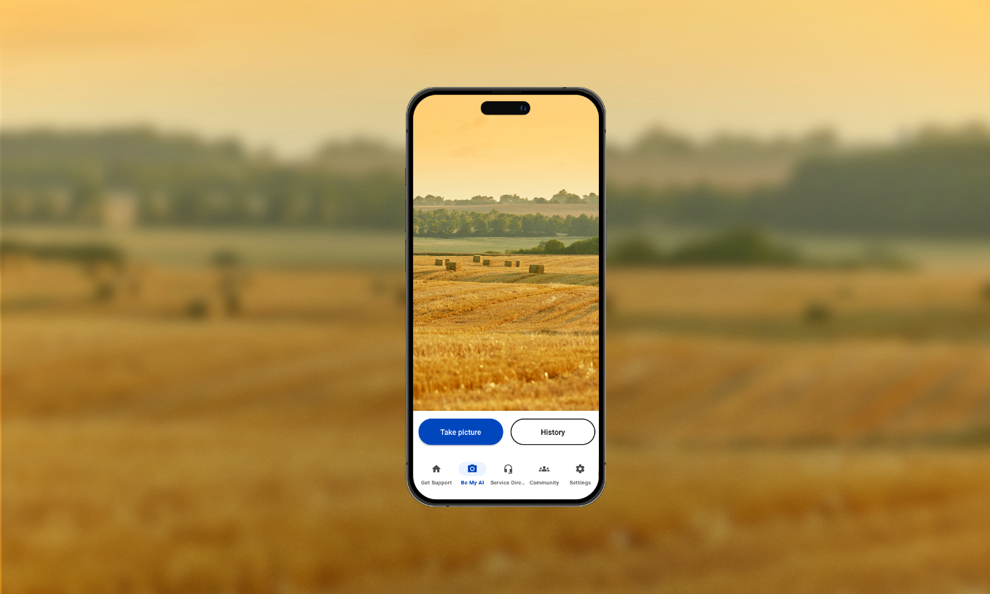 A smartphone displays a photo of a hayfield with bales, matching the blurred landscape of a harvested field in the background.